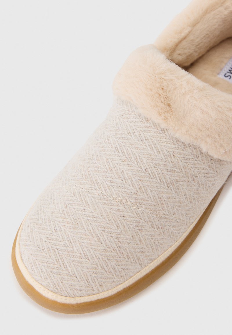 Hellbeige Hausschuhe aus strukturiertem Gewebe mit einem Fischgrätmuster, ausgestattet mit einem plüschigen, weichen Futter aus cremefarbener Kunstfell und einer Gummisohle.