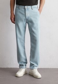 Jasnoniebieskie dżinsy w prostym kroju, z pięcioma kieszeniami i kontrastowym przeszyciem. W połączeniu z białymi trampkami na neutralnym tle.