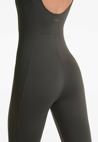 Temno zelena bodysuit z rebrasto teksturo ob straneh. Ima okroglo režo na hrbtu in logo blizu zgornjega dela hrbta. Gladka, prilegajoča se zasnova.