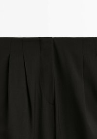 Section de tissu plissé noir avec coutures visibles et plis doux sur un vêtement sur fond blanc.
