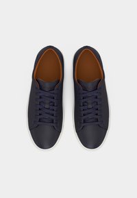 Ζευγάρι σκούρα μπλε δερμάτινα αθλητικά παπούτσια με ταιριαστές κορδόνια και λευκές σόλες, σε θέα από πάνω σε απλό λευκό φόντο.