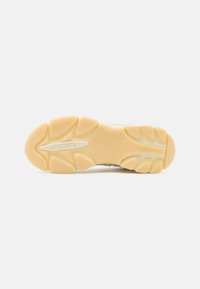 Lacoste sneaker talpa, amely világos bézs színű, texturált gumifelülettel rendelkezik, és cikkcakk mintázatokat tartalmaz, a középen és a sarkán a márkázással.