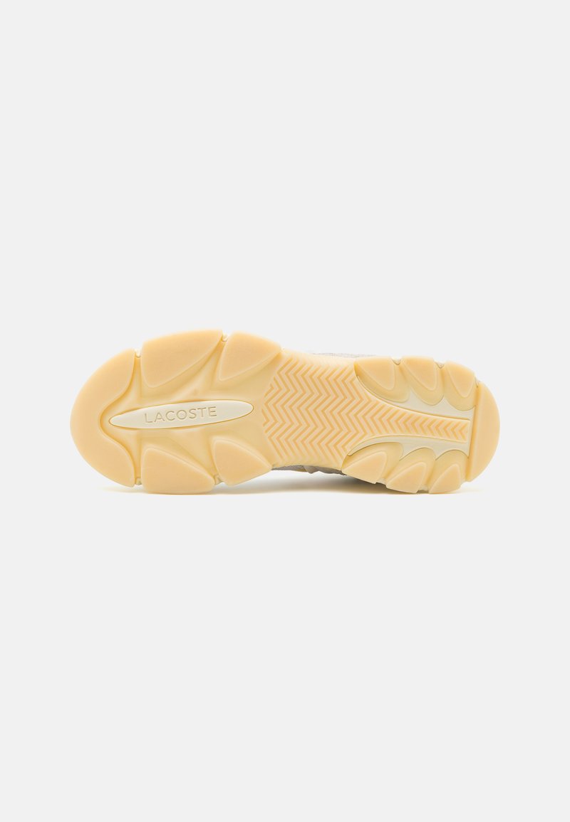 Suela de sneaker de Lacoste, con una superficie de goma texturada en beige claro, con patrones en zigzag y logotipos en el centro y el talón.