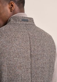 Grau karierter Weste mit strukturiertem Kragen und Logoetikett, die eine weiche Textur und subtile mehrfarbige Faserakzente aufweist.