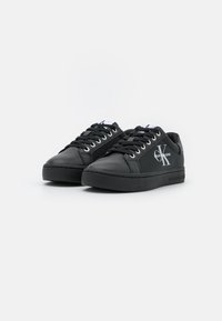 Czarne sneakersy wykonane z gładkiej skóry, z zaokrąglonym czubkiem, sznurowanym designem i białym logo na boku. Charakteryzują się grubą czarną podeszwą.