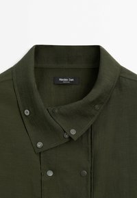 Col de chemise boutonnée vert foncé avec fermetures à pression, présentant une étiquette Massimo Dutti à l'intérieur de l'encolure.