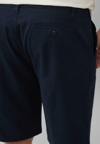 Marineblaue Baumwollshorts mit flachem Frontdesign, Gesäßtaschen mit Knopfverschluss und geradem Schnitt, der knapp oberhalb des Knies endet.
