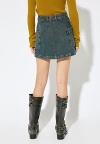 Jeansmini med åtsittande midja, två stora bakfickor och en något utställd fåll. Bärs med höga, svarta läderstövlar med spännen.