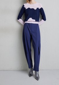 Pull en maille bleu marine avec un motif abstrait rose, associé à un pantalon bleu marine avec des fentes sur les côtés, complété par des bottines à talons pointus argent métallisé.