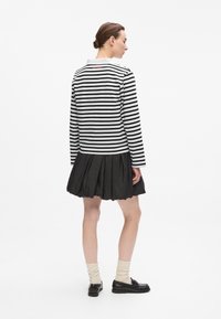 Schwarz-weiß gestreiftes Langarm-Polo mit festem Kragen, kombiniert mit einem voluminösen schwarzen Plisseerock und schwarzen Schuhen.