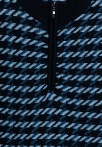 Gebreide trui met een blauw hounds-tooth patroon op een donkere achtergrond, voorzien van een helft-rits kraag en ribgebreide manchetten. Zachte textuur.