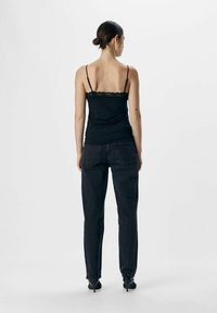 Camisola nera con pizzo, abbinata a pantaloni in denim scuri. La parte superiore ha spalline sottili e l'outfit è completato da scarpe con tacco nere.