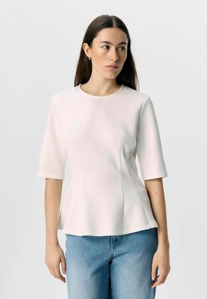 Haut blanc ajusté avec des manches courtes, encolure ronde et design peplum. Texture lisse, coutures minimales et associé à un jean bleu clair.