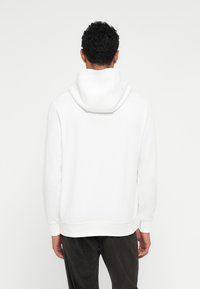 Hoodie branco feito de um tecido suave com um capuz espaçoso, punhos e bainha canelados, exibido pela parte de trás sem logótipos ou padrões visíveis.