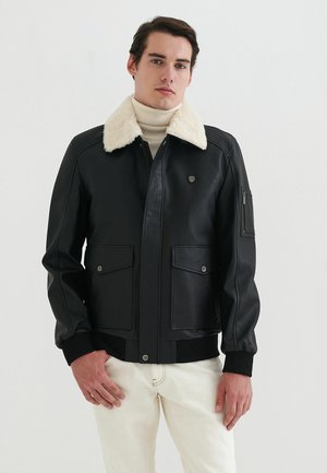 Sort læderjakke med en beige faux fur-krave, front lynlås, to store brystlommer og en lynlåslomme på ærmet.