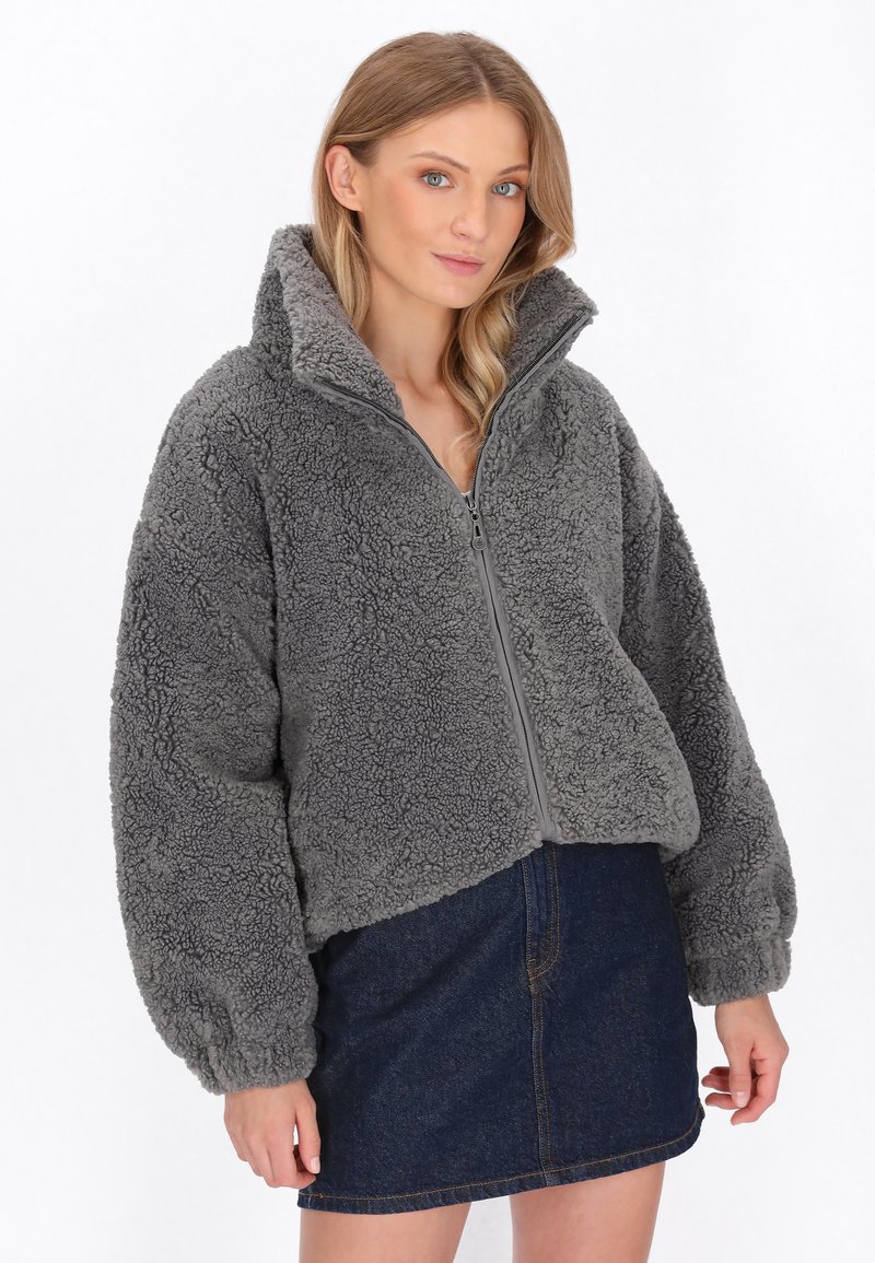 Grå fleecejakke med høj krave, frontlynlås og voluminøse ærmer, parret med et denimskørt for et afslappet look.