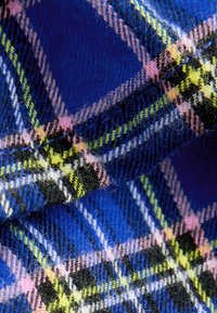 Tissu à carreaux bleu présentant un motif de lignes croisées en noir, rose et vert, avec une texture douce et une apparence chaleureuse.