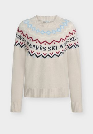 Bežs adīts džemperis ar garām piedurknēm. Iezīmē krāsu bloku rakstu zilonī, sarkanā un melnā krāsā, ar tekstu "APRÈS SKI" ap kakla laukumu.