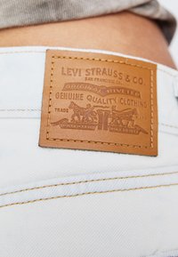 Barna bőr folt, dombornyomott logóval világoskék farmeren, varrási és szegecsmintákkal. A felirat: "Levi Strauss & Co."
