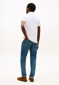 Hvit kortermet poloshirt, blå denimjeans, brune sko; designet med en avslappet passform, enkel silhuett og minimal detaljer.