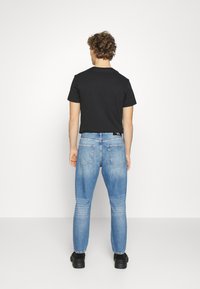 Zwarte cropped t-shirt gecombineerd met lichtblauwe denim jeans. De jeans hebben een slim fit en ronde achterzakken. Zwarte schoenen maken de look af.