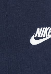 Material bleumarin cu o textură netedă, având un logo Nike brodat alb într-un design dinamic de swoosh.