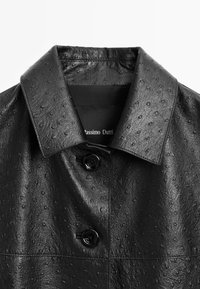 Černá kožená bunda s hladkým povrchem, širokým límcem, dvěma černými knoflíky a jemným embosovaným vzorem.