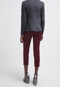 Šedý přiléhavý blejzr s dlouhými rukávy, doplněný vínovými zkrácenými kalhotami. Stříbrné sandály na podpatku outfit dokončují.