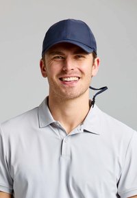 Cappello da marina con un design strutturato, dotato di una visiera curva e una tracolla regolabile, indossato con una polo grigia chiara. Vestibilità rilassata e texture morbida.
