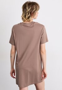 Barna, rövid ujjú, lágy és sima anyagból készült pólóruha, laza szabással és kerek nyakkivágással.