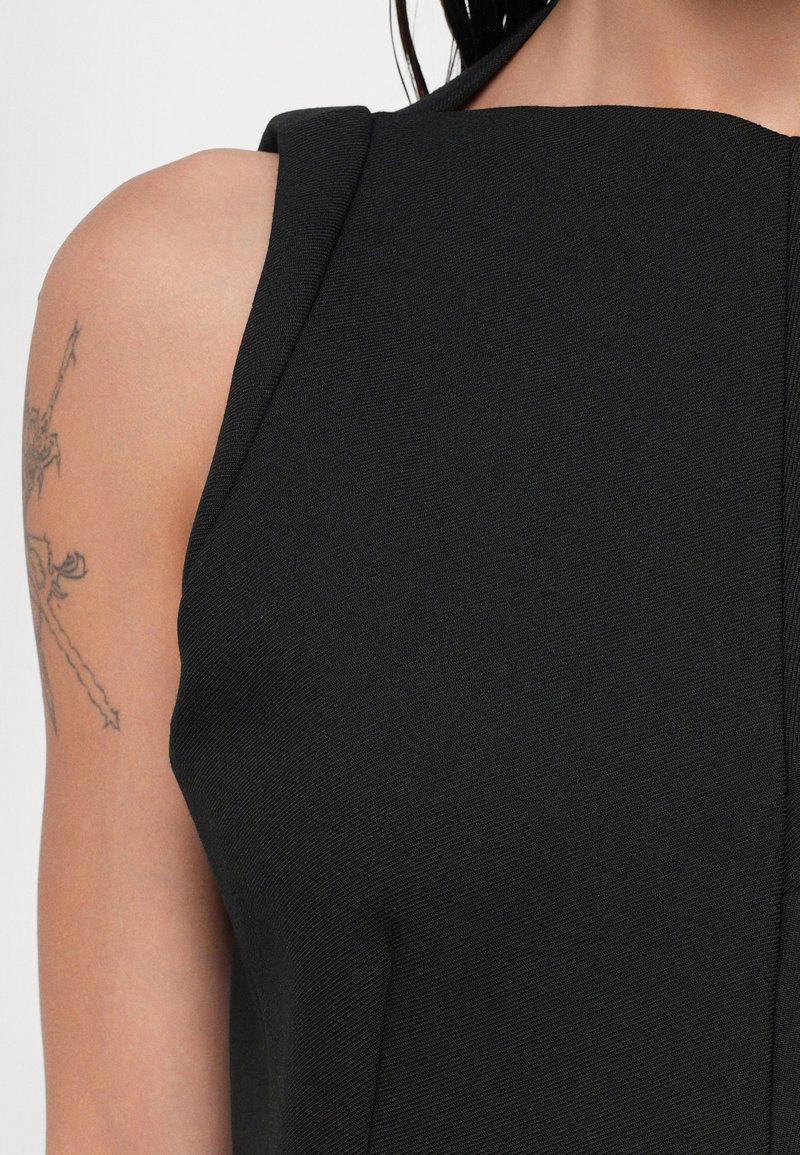 Svart ärmlös klänning med en strukturerad halsringning, texturerad tyg och detaljer i sidsömmarna. Exponerad dragkedjestängning längs fram.