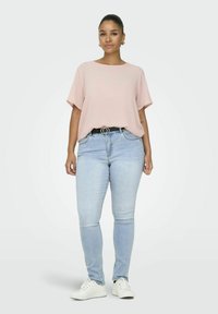 Różowa bluzka krótki rękaw, jasnoniebieskie dżinsy skinny z czarnym paskiem z podwójną klamrą O-ring oraz białe trampki.