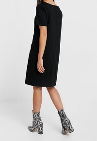 Černé krátké šaty s uvolněným střihem a zipem na zadní straně. Spárováno s vysokými hadími botami na podpatku v černé a bílé barvě.