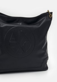 Czarna skórzana torba z zaokrąglonym spodem; posiada wytłoczone okrągłe logo oraz górny zamek błyskawiczny; gładka tekstura o matowym wykończeniu.