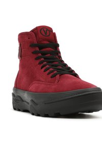 Baskets montantes en suédine rouge avec des lacets noirs, une semelle en caoutchouc texturée et un patch logo sur le côté, arborant un design à plateforme épaisse.