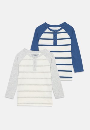 Deux chemises pour tout-petit à manches longues avec des rayures horizontales, l'une avec des manches bleues et des rayures bleues, l'autre avec des manches grises et des rayures grises.