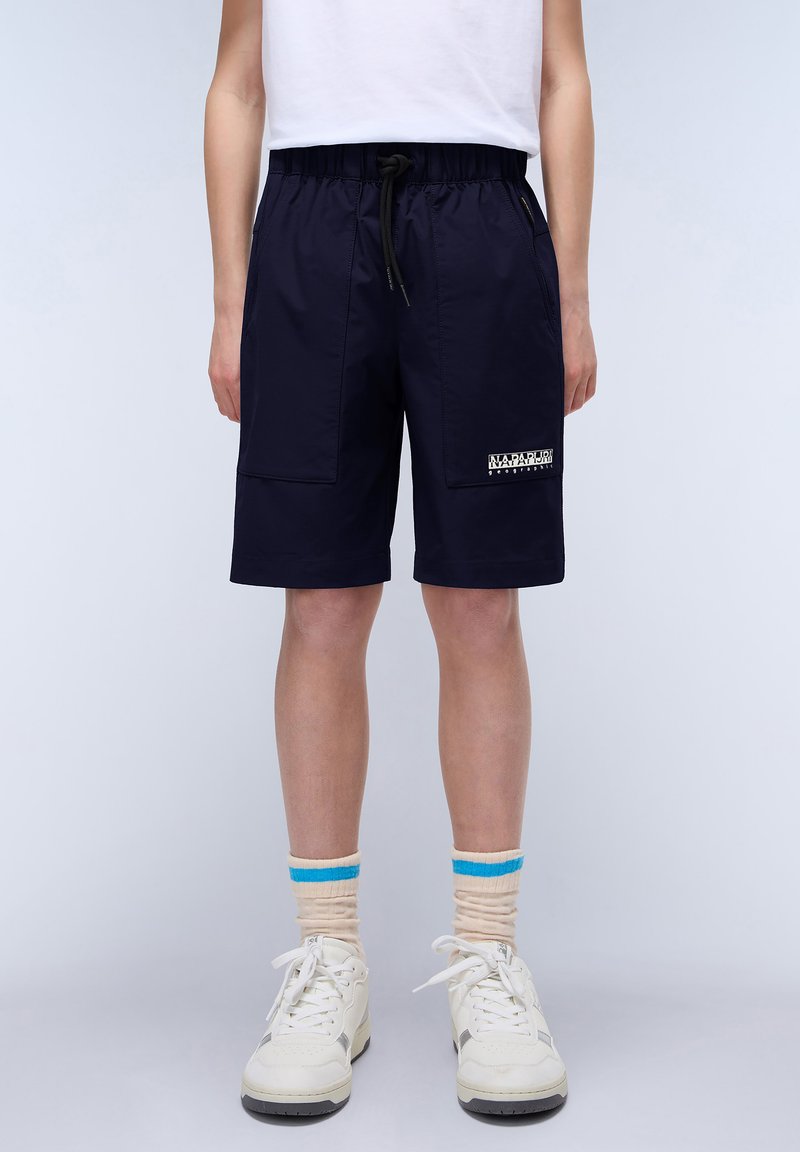 Marina shorts med elastisk midjeband och dragsko. Har sidofickor och en logotypetikett. Bärs med vita sneakers och randiga beige strumpor.