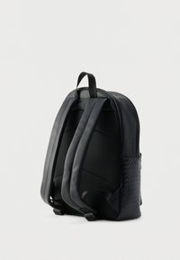 Sac à dos noir alliant cuir lisse et maille texturée. Motif tissé remarquable sur le côté, bretelles rembourrées et poignée supérieure incluses.