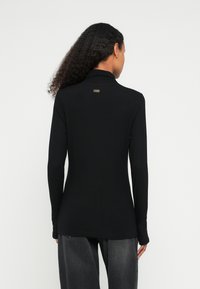 Czarny, długi top z golfem i gładką fakturą, zdobiony małym metalicznym logo z tyłu oraz dopasowanym krojem.