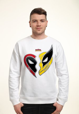 Man wearing white sweatshirt with red and yellow heart-shaped Deadpool and Wolverine masks and "Best Friends" text on chest.