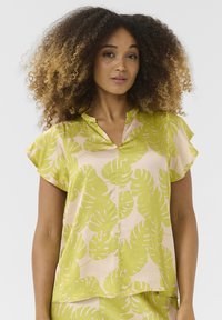 Blusa a maniche corte in tessuto rosa chiaro con grande stampa di foglie di monstera verdi, caratterizzata da una vestibilità rilassata e un design con colletto a scollo.
