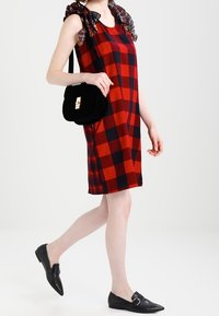 Rot-schwarz karierte ärmellose Kleid mit einem karierter Akzent an den Schultern, kombiniert mit einer schwarzen Wildleder-Umhängetasche und schwarzen Ballerinas.