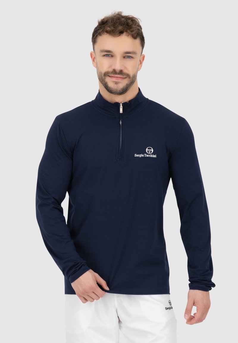 Maglietta a maniche lunghe con zip di colore blu navy, realizzata in tessuto morbido. Presenta un colletto alto e un logo bianco sul petto. Design semplice, stile aderente.