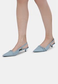 Kék slingback cipők hegyes orral, vékony boka pánttal és kis sarkával. Simább, fényes anyagból készültek.
