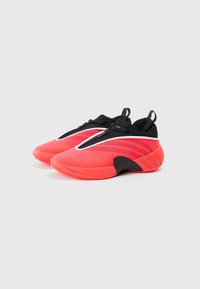 Une paire de baskets modernes rouges et noires à enfiler avec fermeture à glissière et languettes de tirage sur fond blanc.