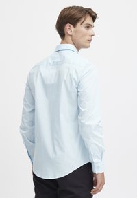 Helles blaues Langarmhemd aus glattem Stoff, mit spitzem Kragen, Knopfmanschetten und abgerundetem Saum hinten.