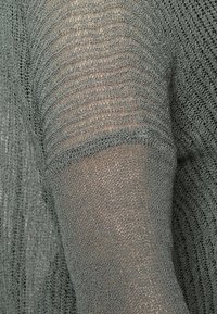 Suéter gris de punto con un diseño texturizado y finas rayas verticales. Mangas largas con un aspecto ligeramente transparente.