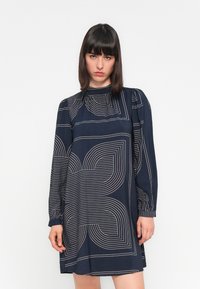 Vestito blu navy con maniche lunghe, collo alto e motivi geometrici a linee bianche. Presenta una vestibilità ampia e una texture morbida.