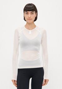 Hvid langærmet mesh-top med rund halsudskæring, der har et struktureret mønster og en tætsiddende pasform, lagdelt over en simpel hvid tanktop.