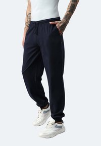 Marineblaue Jogginghosen mit elastischem Bund, Seitentaschen und gerippten Bündchen, kombiniert mit weißen Sneakern mit grauen Akzenten.